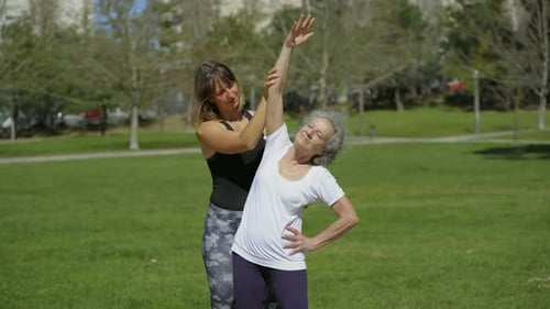 Smiling Senior Woman Training with Coach on Green Lawn