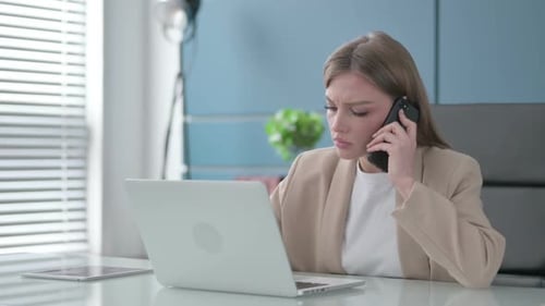 Businesswoman Talking on Phone While Using Laptop in Office