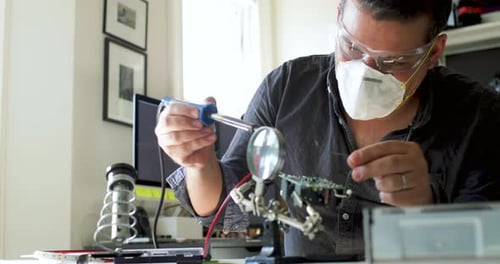 Focused Adult Soldering a Circuit Board at Home