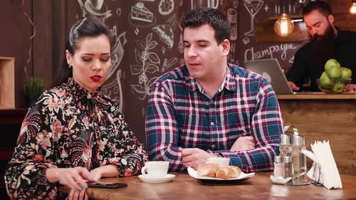 Couple on a Date in Stylish Coffee Shop Pub Restaurant Drinking Coffee and Looking on Smartphone
