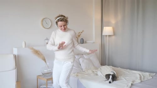 Woman Dancing with Headphones and a Dog in Bedroom
