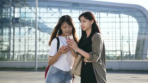 Charming Young Asian Girls in Casual Clothes with Phones Standing Near the Airport