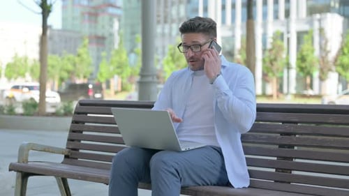 Man Using Laptop and Talking on Phone Outdoors
