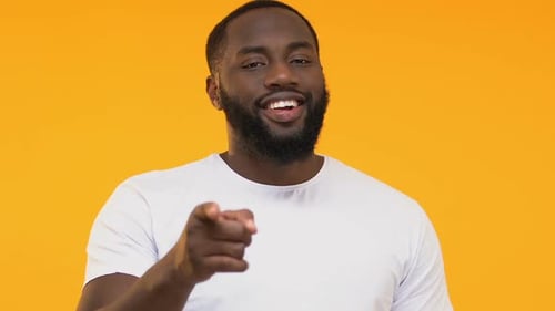 Fröhlicher afroamerikanischer Mann zeigt mit dem Finger auf die Kamera und zwinkert, Ich wähle dich