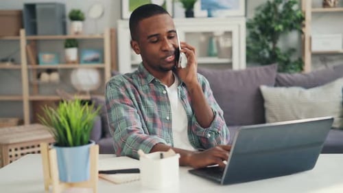 Young Adult Working at Home Using Laptop and Phone