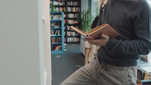 Mittelteil eines männlichen Uni-Studenten beim Lesen eines Buches in der Bibliothek
