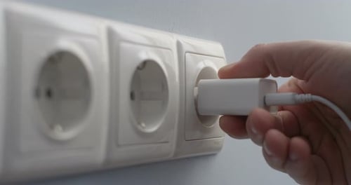 Hand Plugging White USB Wall Charger into Outlet