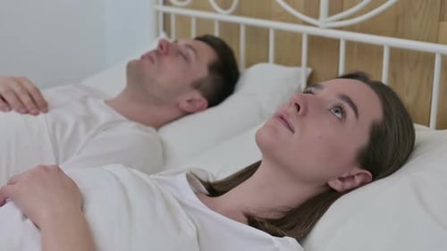 Beautiful Woman Awake in Bed Next to Sleeping Partner