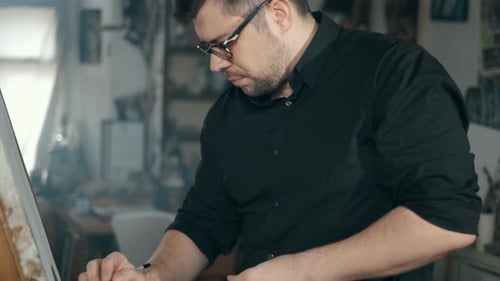 The Artist Is Working on a Painting on the Easel in the Workshop with a Pencil