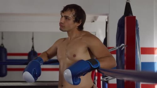 Young Boxer Leaning on Ropes in Boxing Ring