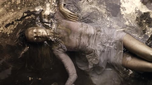 Young Model Woman Is Lying in Shallow of Pool with Water with Golden Dye Painted Face and Hair