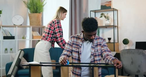 Fille rassemblant des boîtes en carton sur le canapé tandis que l'étagère pliée mesure un gars confiant