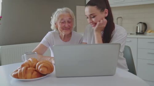 Grandmother and Granddaughter Using Laptop at Kitchen Table