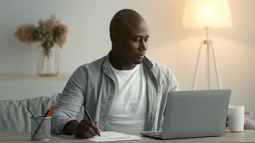 African Man Taking Notes Having Coffee Sitting At Laptop Indoor