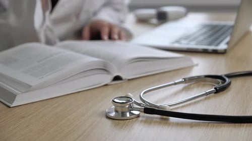 Close Up View of Stethoscope Medical Equipment with Female Doctor Reading the Book in the Background