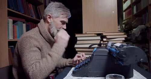 Un viejo escritor con barba gris y un lápiz detrás de la oreja usa una máquina de escribir