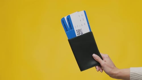 Hand Holding Passport and Airline Tickets on Yellow