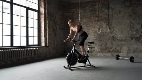 The woman in sport clothes is working out on the exercise bike in the green gym