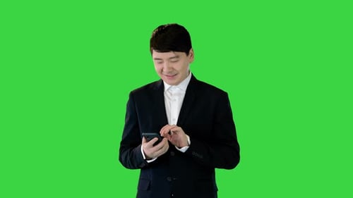 Asian Man in Suit Smiles While Using Mobile Phone on a Green Screen Chroma Key