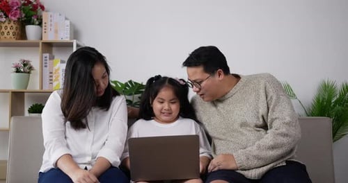 Young father and mother teaching lovely daughter use laptop computer