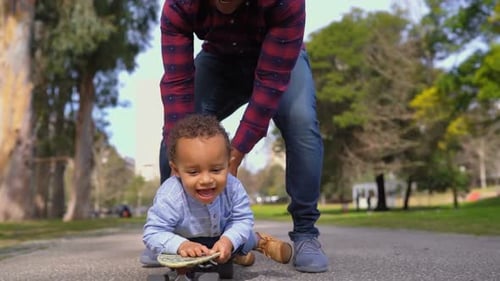 Baby Rides Skateboard with Dad in Park