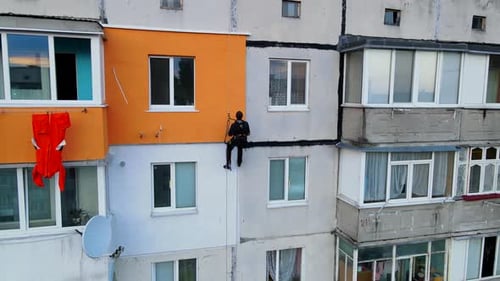 Pintura e decoração de edifícios. Trabalhador em um canteiro de obras de um prédio alto. Perigoso