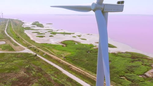 Large Blades Rotate on Windmills Near Pink Lake in Summer