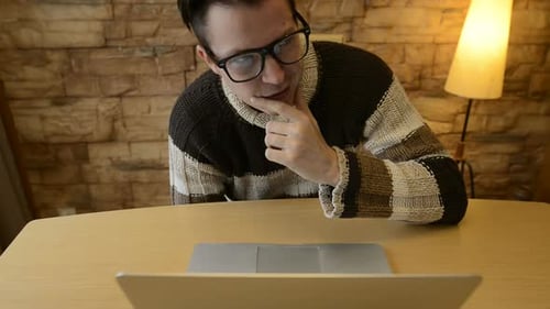 Glücklicher junger Mann denkt und stellt sich vor, während er Laptop zu Hause benutzt