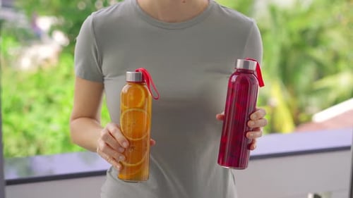 Une femme tient deux bouteilles avec une boisson au kombucha dans ses mains qui ont différentes saveurs d'orange et