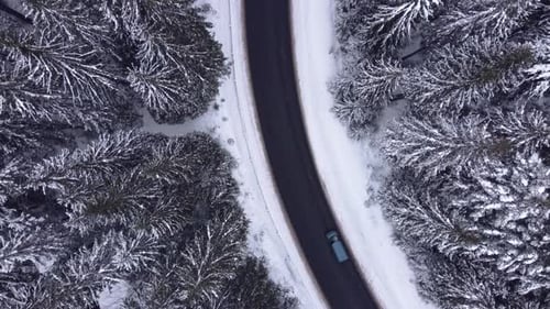 Aerial top view snowy forest mountains with cars driving winter road.