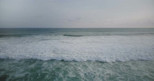 Drone Flying Towards Big White Foamy Ocean Wave Reaching the Shore and Crashing, Creating Amazing