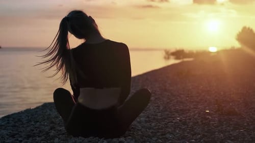 Femme assise en position du lotus pratiquant le yoga matinal sur la plage