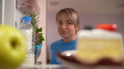 Woman Choosing Apple Over Cake in Refrigerator