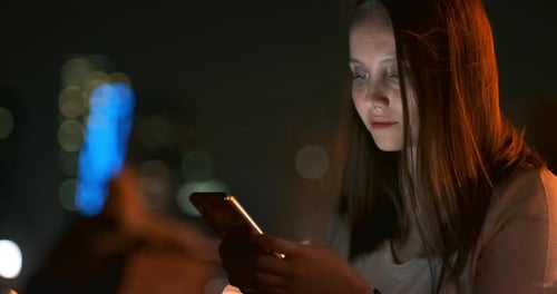 Ein junges Mädchen auf dem Hintergrund der Nachtstadt schaut in den Smartphone-Bildschirm