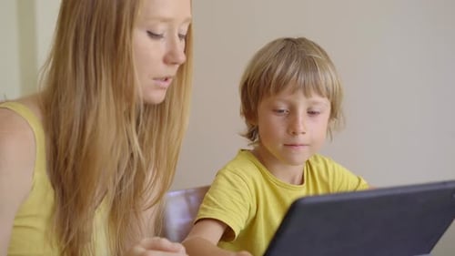 A Young Woman and Her Little Son Sit a Home During Quarantine and Study in the Internet School Using