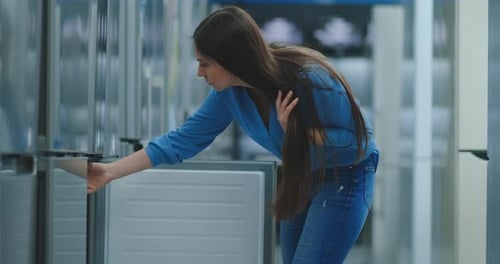 A Young Woman To Open the Refrigerator Door To Store Appliances and Compare with Other Models To Buy
