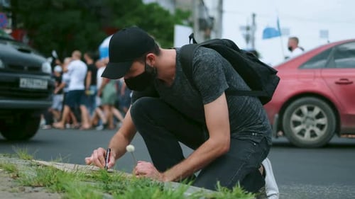 Man Kneeling to Write on Cardboard at Roadside
