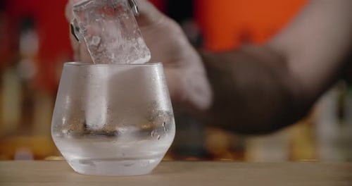 Bartender Puts Big Ice Cube to the Frozed Cocktail Glass By Forceps Making the Cocktail in the Bar