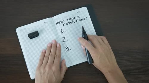 Hands Writing New Year's Resolutions in Notepad