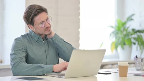Man Works on Laptop and Rubs Neck