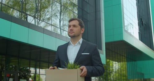 Businessman in Despair Lost Job and Walking Near Office Center with Carton Box and Documents with a