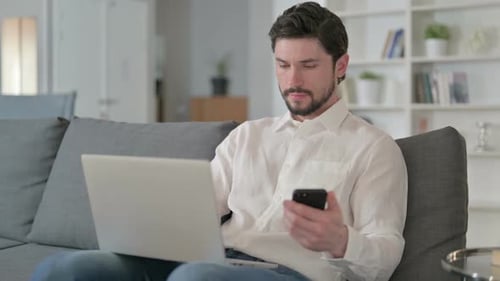 Man Working on Laptop and Using Smartphone