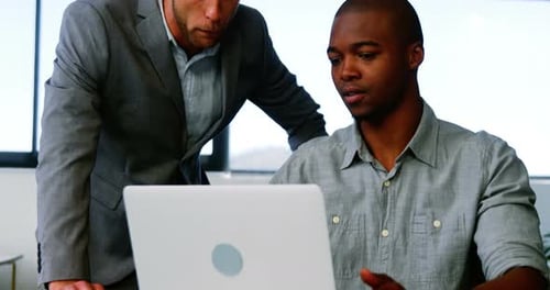 Two Men Reviewing Laptop in Bright Office Setting