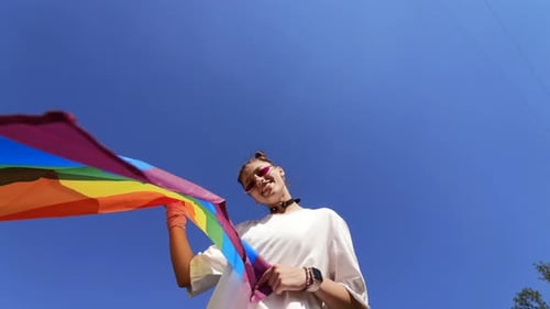 Young Person Holding Rainbow Flag Against Blue Sky