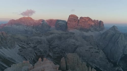 Aerial view flying above jagged Tre Come South Tyrol mountain range valley terrain with sunlit orang