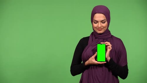 A Muslim Woman Shows a Smartphone with Green Screen to the Camera with a Smile Green Screen