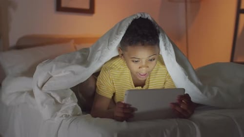 Garçon afro-américain jouant sur une tablette au lit le soir