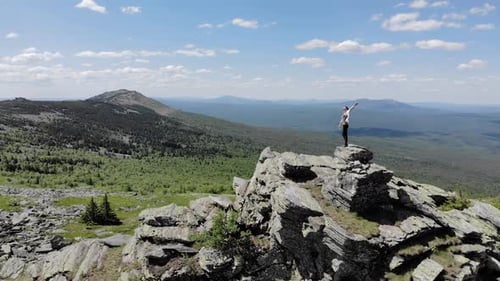 A Girl Stands on Top of a Mountain on the Rocks and Looks Into the Distance, Aerial Video