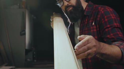 Bearded Woodworker Inspecting Piece of Wood in Workshop