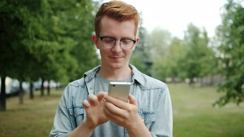 Young Man Using Smartphone in Park Touching Screen Enjoying Modern Device